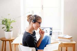 Junges Mädchen sitzt am Schreibtisch und hört mit ihren Kopfhörern Musik.