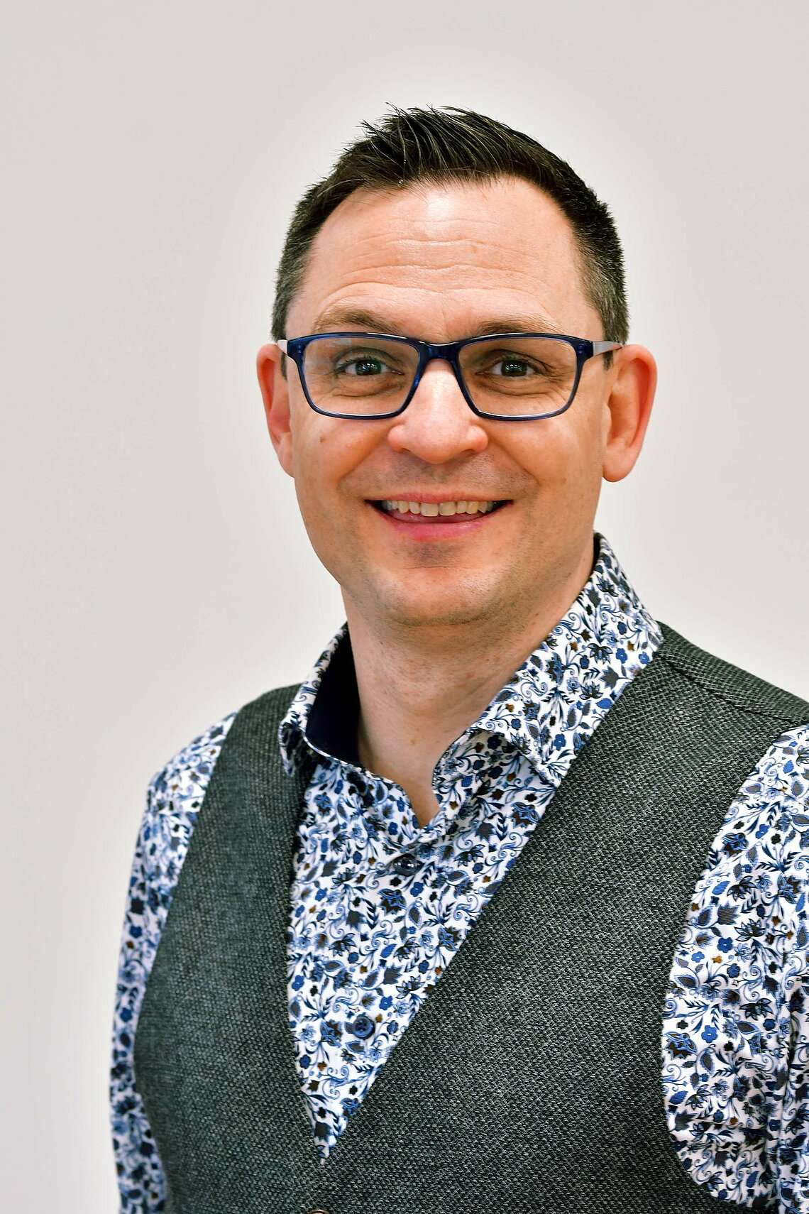 Ein Mann mit Brille, buntem Hemd und einer dunklen Weste
