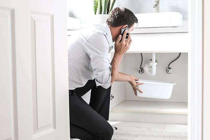 Ein Mann sitzt im Bad in der Hocke und ruft die Servicehotline an.