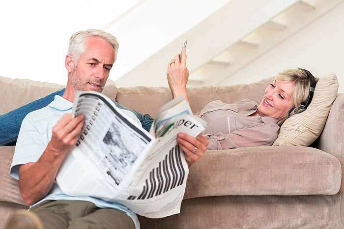 Ein Ehepaar liest gemeinsam Zeitung im Wohnzimmer.