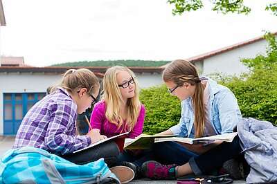 Drei Mädchen mit Brille sitzen vor der Schule und lernen.