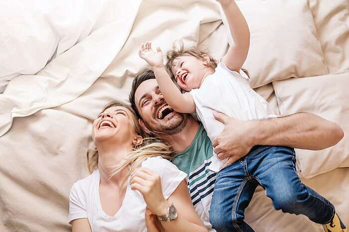 Mutter, Vater und Kind tollen zusammen im Bett herum.
