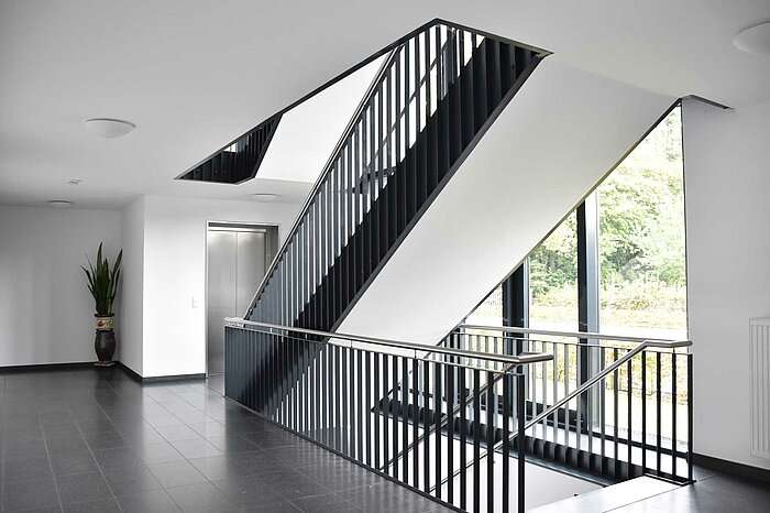 Ein Treppenhaus in einem Neubau mit dunklem Boden, weißen Wänden und schwarzen Treppen.